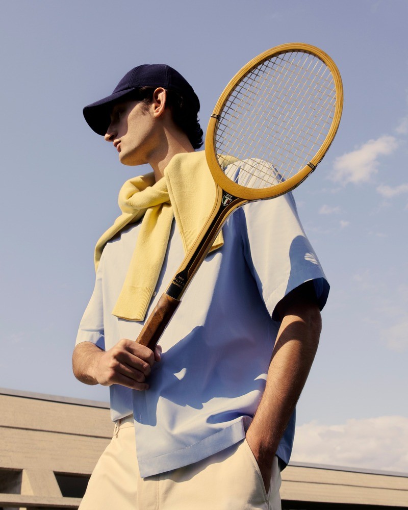 Ready for a casual tennis match, Aaron Shandel wears a Mytheresa outfit featuring JACQUEMUS pants, a Lardini poplin short-sleeve shirt, and a Giorgio Armani cap.