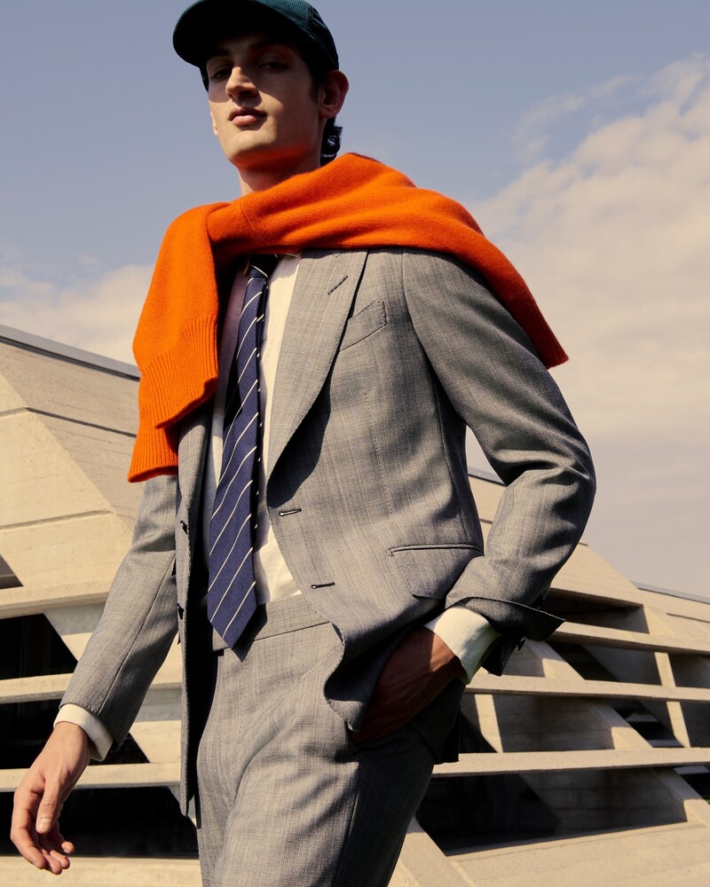 Aaron Shandel exudes sophistication in a grey Tom Ford suit, complemented by an orange Allude sweater and an Acne Studios cap.