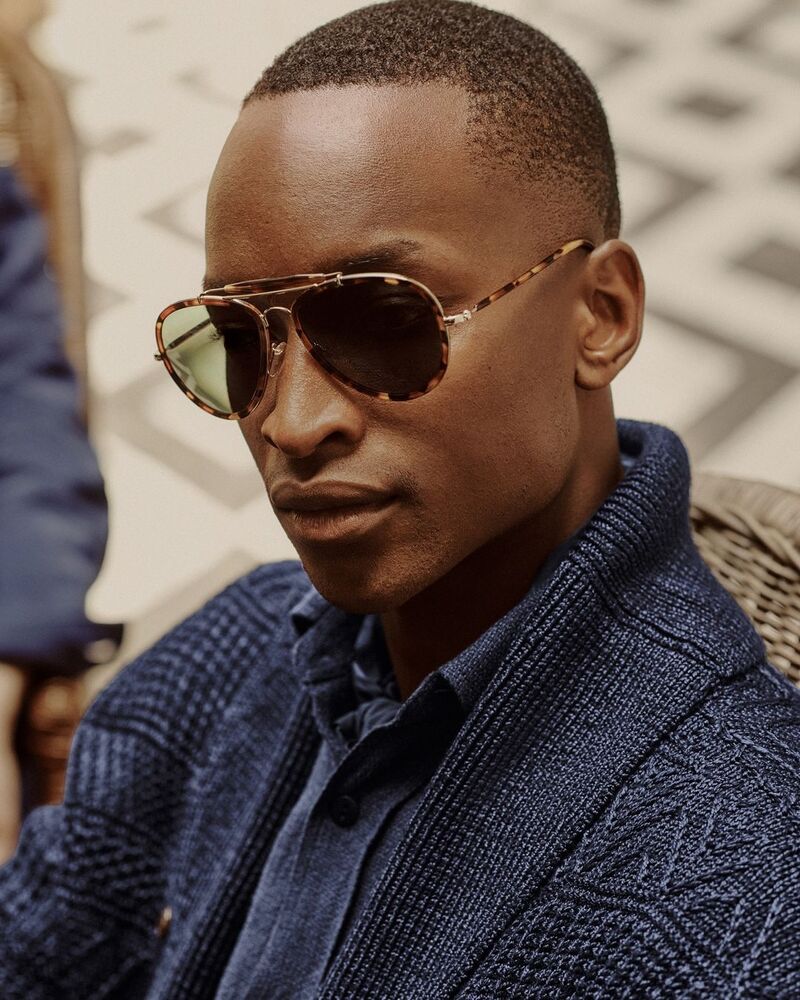 Oliver Kumbi embraces monochromatic style in a woven shirt and shawl neck cardigan from the Ralph Lauren Purple Label spring-summer 2024 collection. 