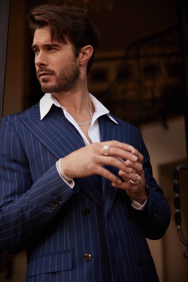 Alex Prange showcases Smiling Rocks jewelry—a chain necklace, bracelet, and statement rings—in a sharp pinstripe suit.