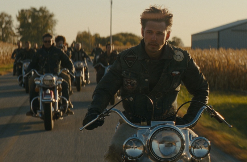 Austin Butler as Benny leads a group of bikers in The Bikeriders, donning a rugged leather jacket with patches.