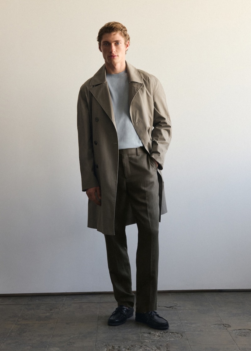 Valentin wears a trench with a sweater, pleated trousers, and black leather driving shoes
