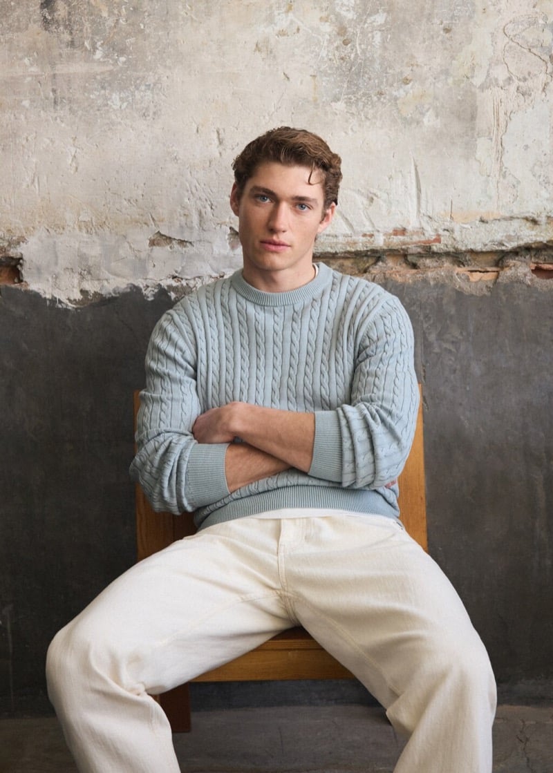 Valentin wears an aqua green cable-knit sweater with ecru jeans