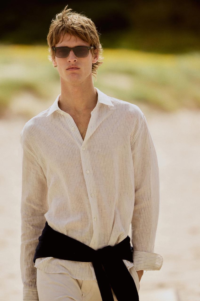 Yeray wears an off-white striped linen shirt with a sweater tied at his waist