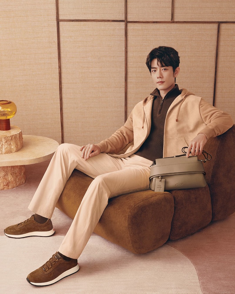 Xiao wears a camel hoodie over a brown half-zip knit with cream trousers and olive-brown sneakers