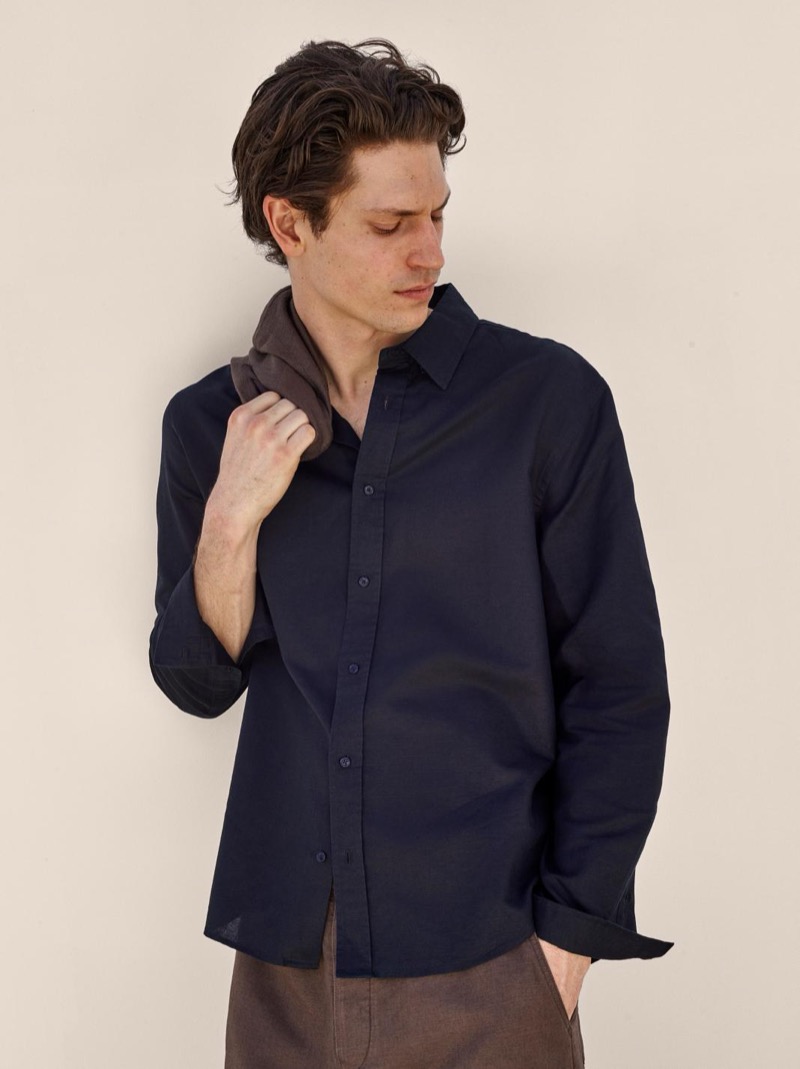 Justin wears a navy linen button-down shirt with brown trousers