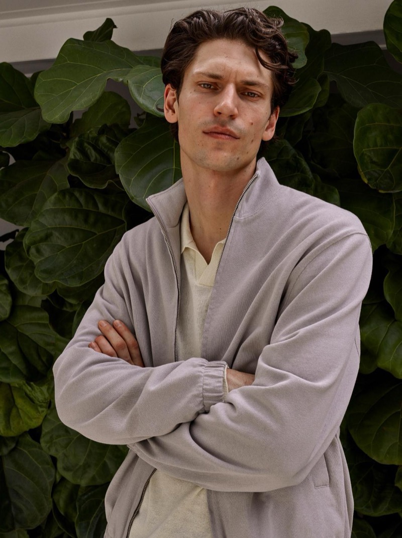 Justin wears a gray full-zip mock-neck sweatshirt over a cream polo against tropical foliage