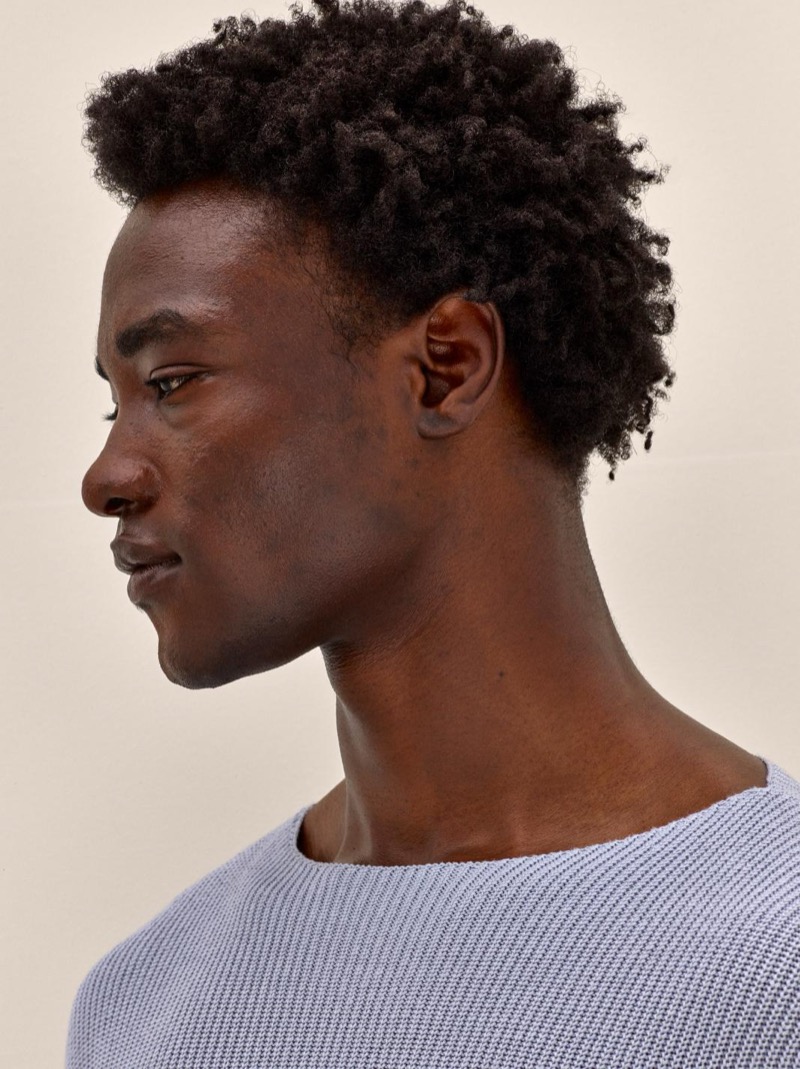 George in a close-up portrait wearing a light blue textured crew-neck knit sweater