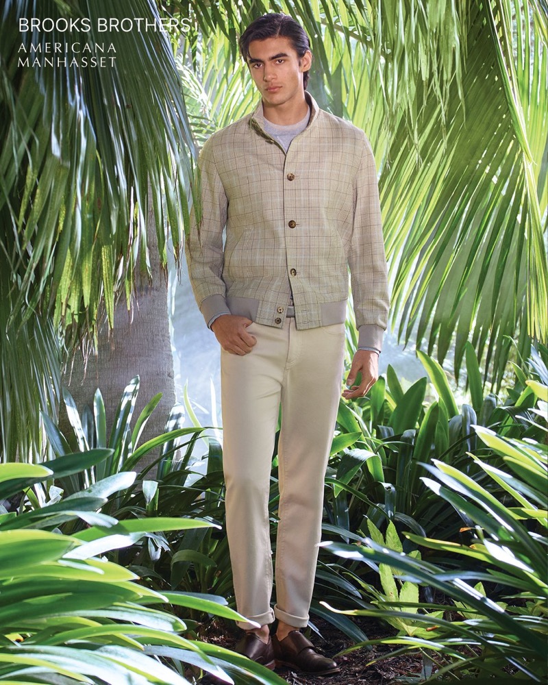 Akbar wears a Brooks Brothers plaid bomber jacket over cream chinos with brown loafers