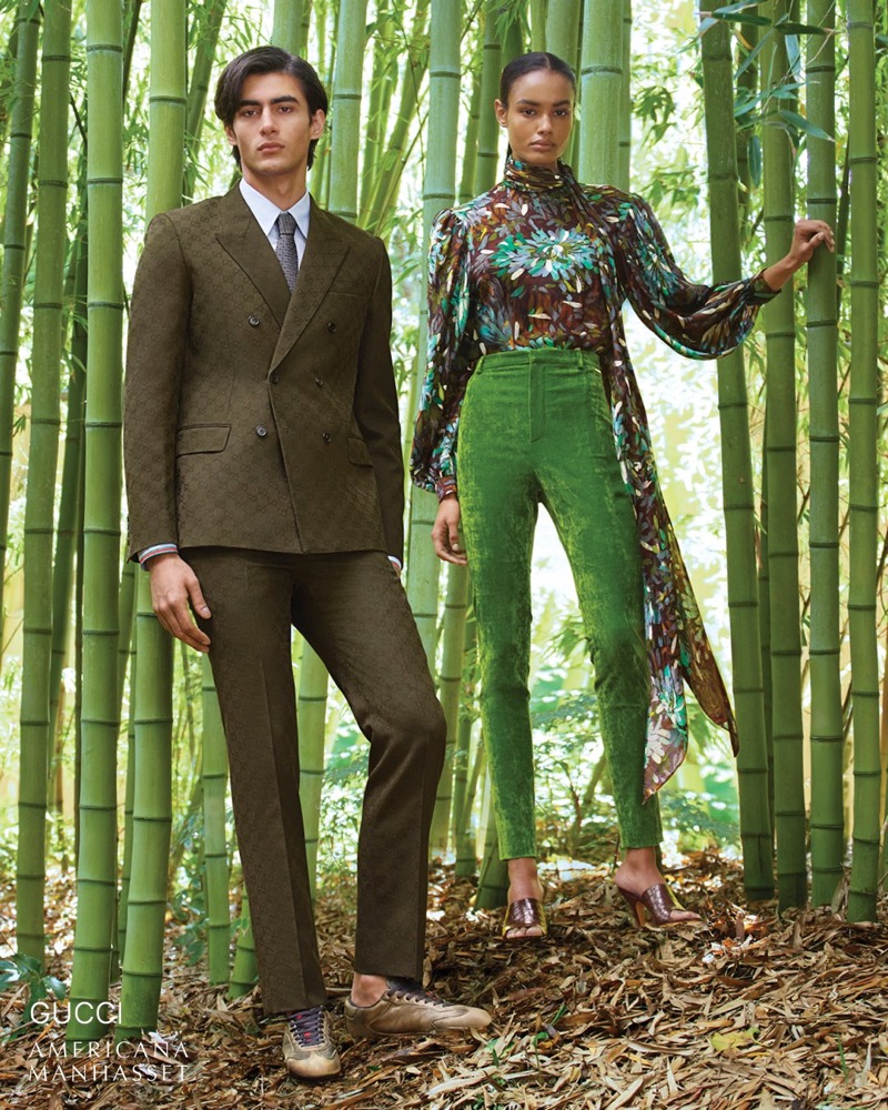 Akbar wears a Gucci olive GG-monogram double-breasted suit with a dress shirt and tie alongside Ana Beatriz in green floral among bamboo