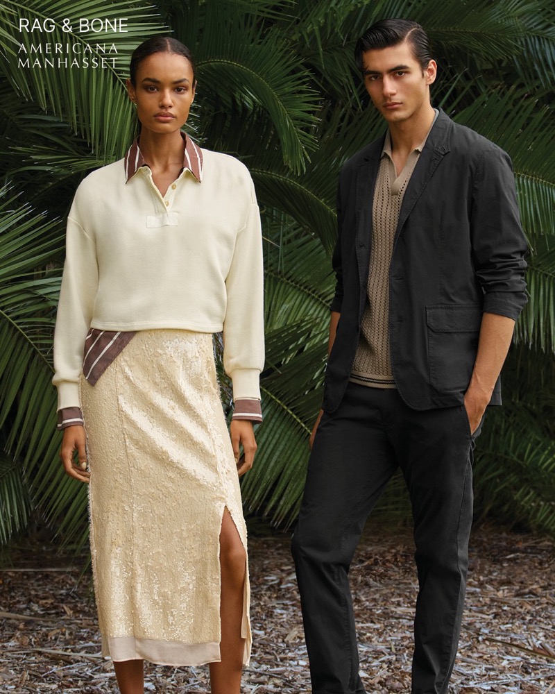 Akbar wears a rag & bone dark blazer over a knit polo with dark trousers alongside Ana in a cream polo sweater