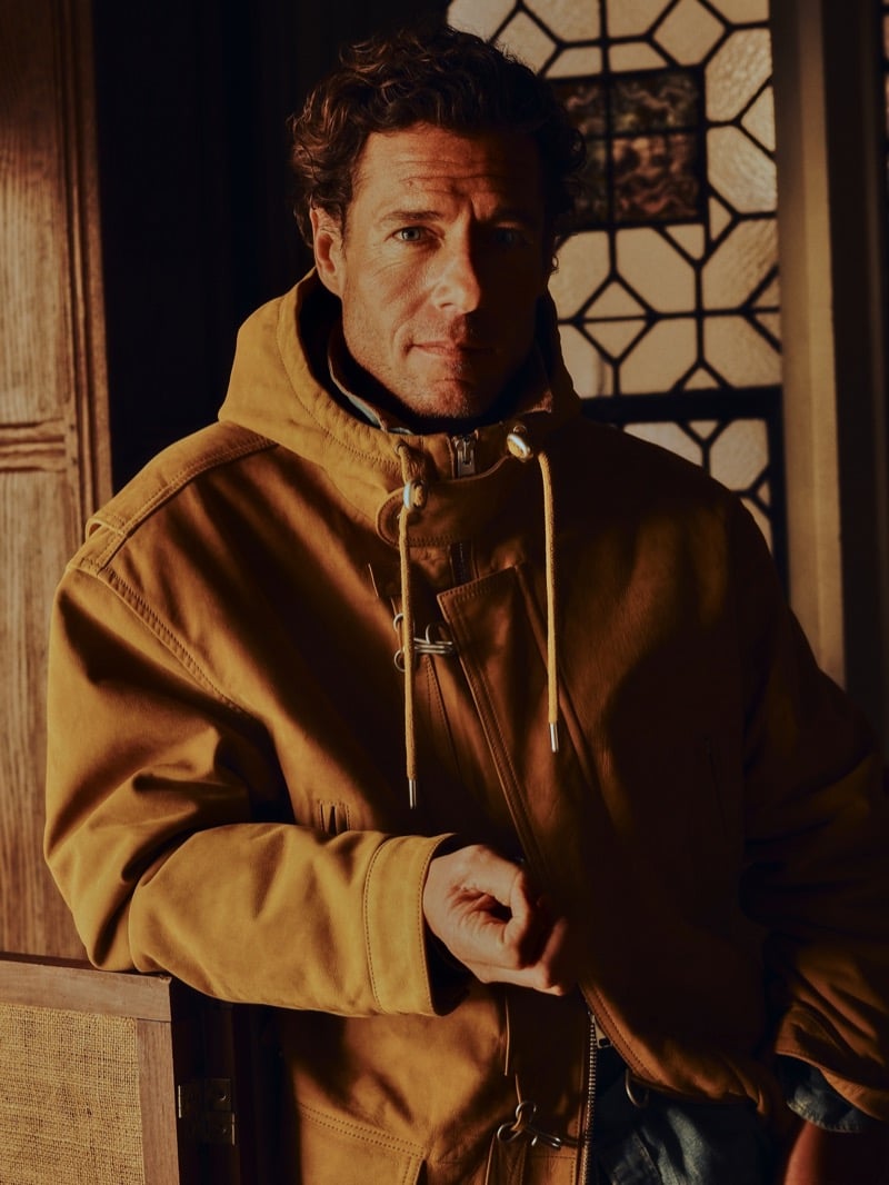 Phillips wears a nubuck leather fireman's jacket with drawstring toggles and metal clasps, photographed against a leaded stained glass window for Banana Republic's Archive Reissue collection