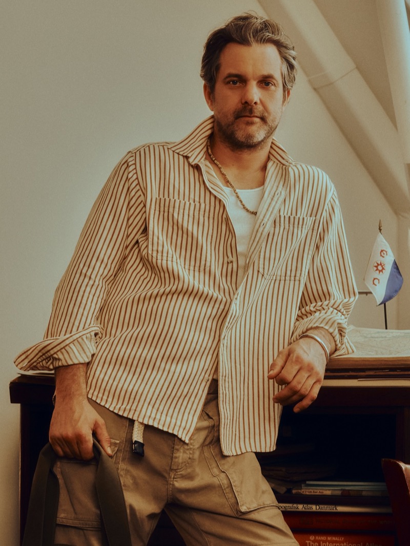 Jackson wears a cream and brown vertical-striped cotton hemp shirt over a white tank with khaki cargo trousers, leaning against a desk with an Explorers Club pennant for Banana Republic's Archive Reissue collection