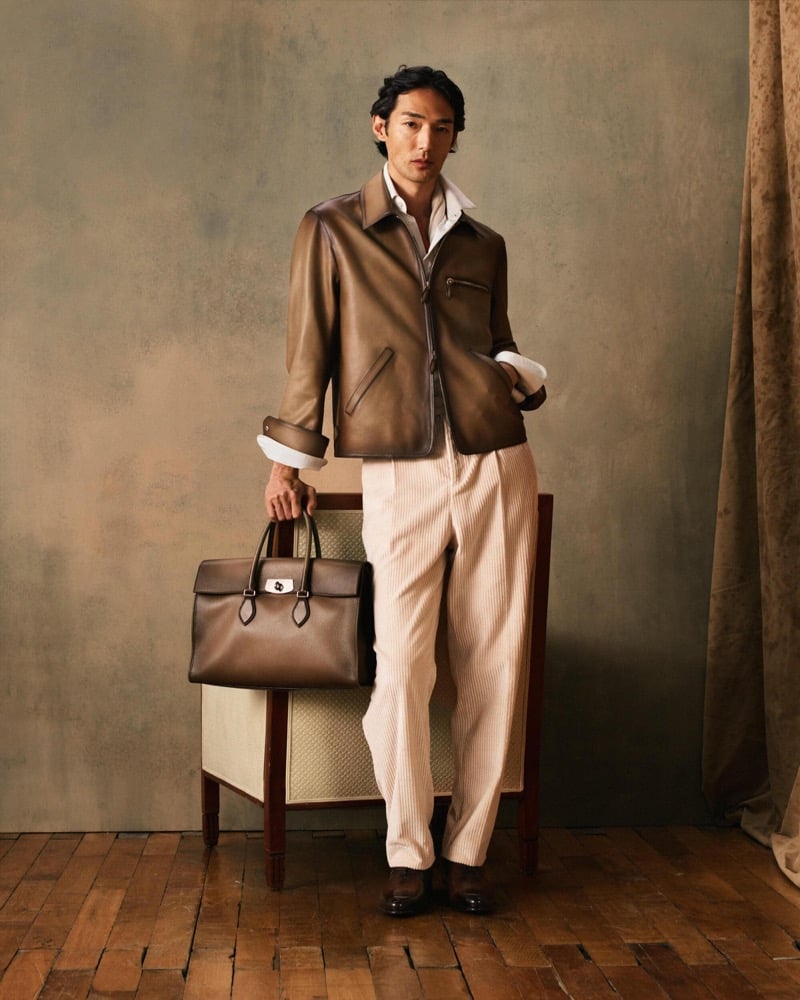 Naoki stands beside a chair in a taupe leather jacket over a white shirt with ivory wide-leg trousers and a brown leather bag