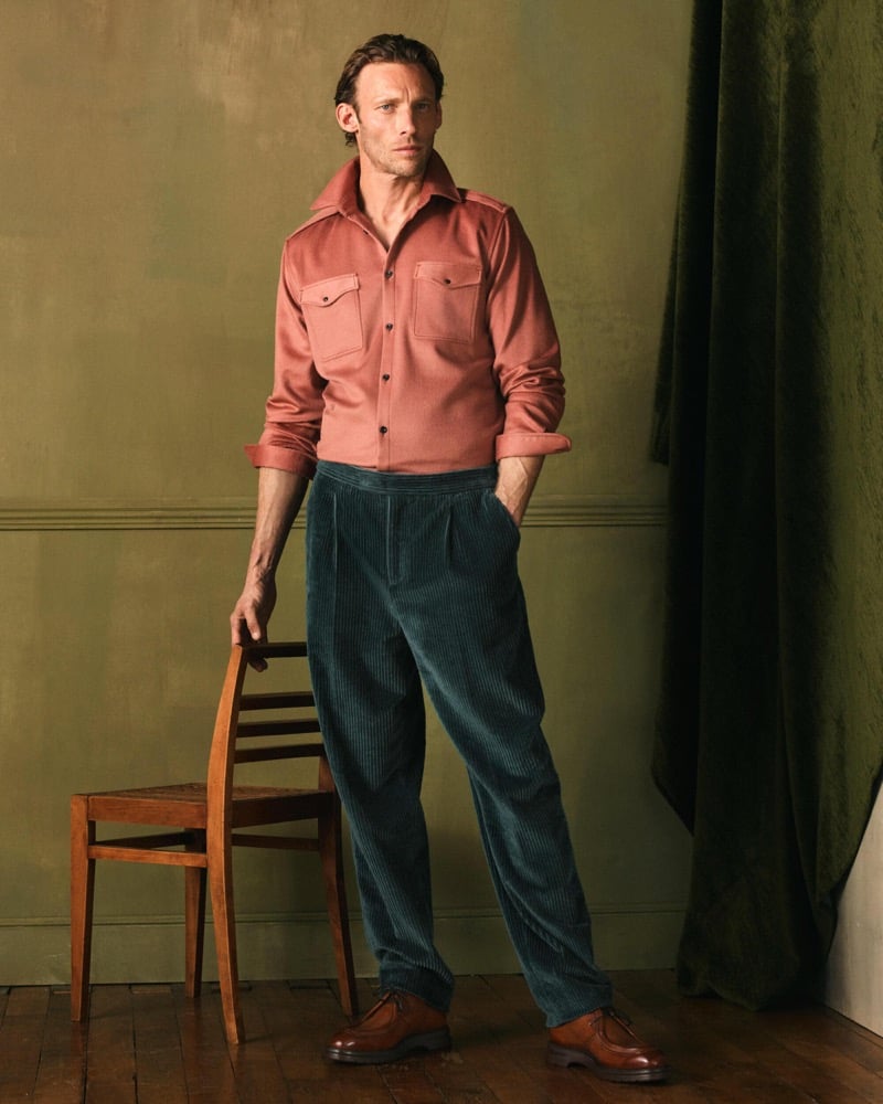 Arnaud stands beside a chair in a vintage pink western-style shirt with teal corduroy wide-leg trousers and cognac leather shoes