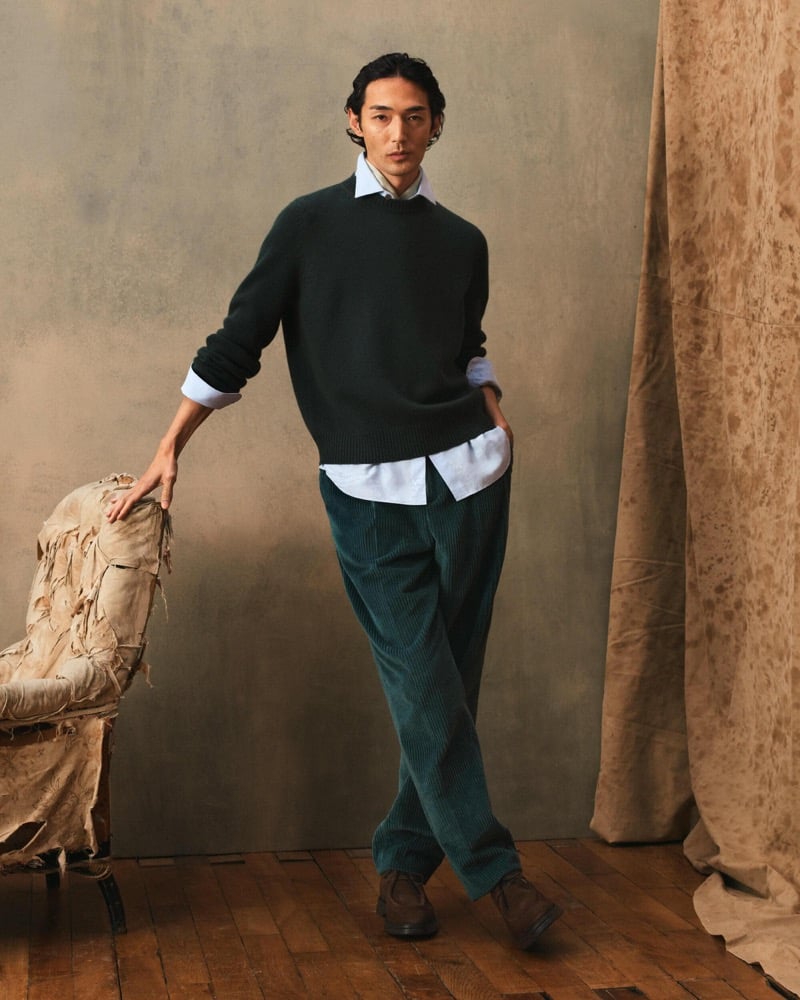 Naoki wears a dark green crewneck sweater over a white shirt with teal corduroy trousers and suede shoes