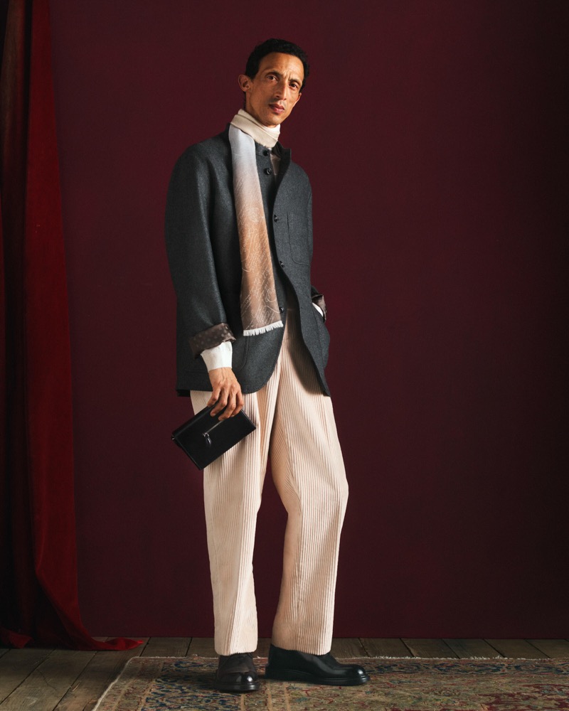Naoki wears a charcoal jacket with an ombre scarf over ivory pinstripe wide-leg trousers with a small black leather clutch and dark boots