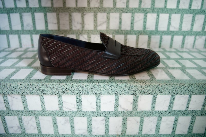 A dark brown basket-weave penny loafer sits on green-veined marble tile