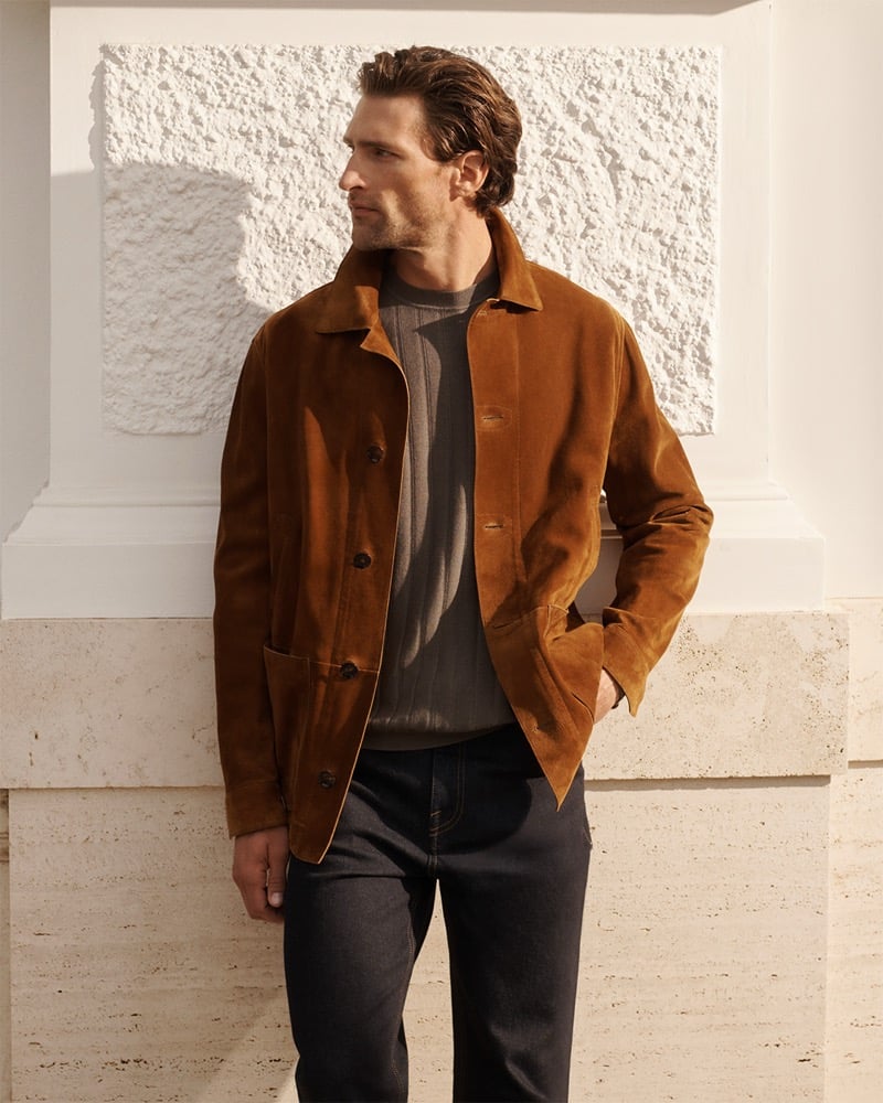 Fabrizio wears a Brioni rust suede jacket over a gray ribbed sweater with dark trousers against a textured white wall