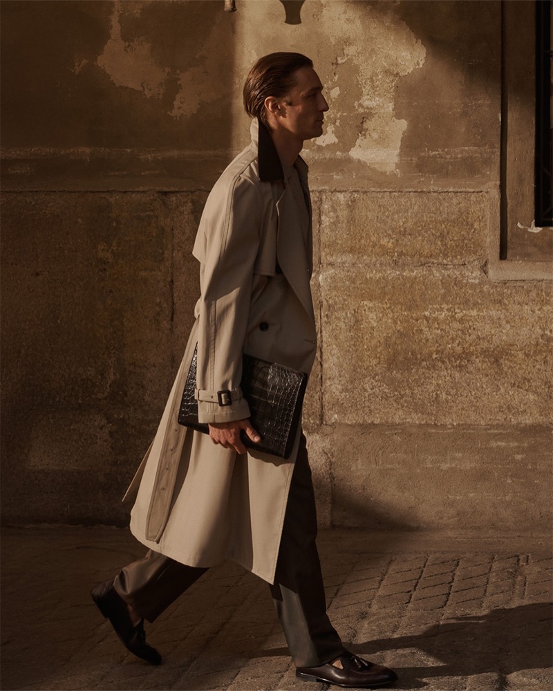 Fabrizio wears a pale Brioni trench coat and carries a dark crocodile-embossed leather clutch on a Roman cobblestone street