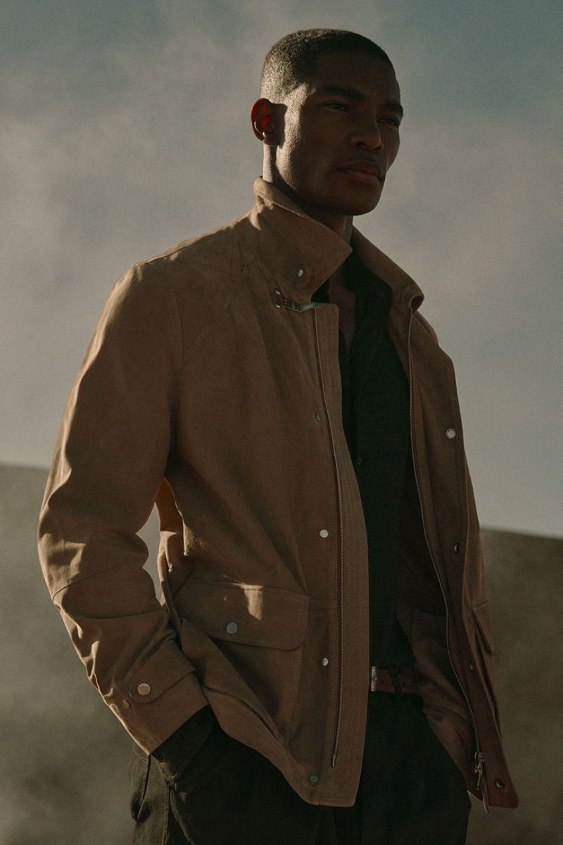 Niyo wears a tan suede jacket over a dark shirt