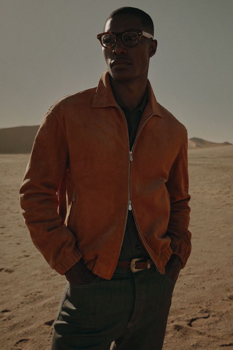 Niyo wears a burnt orange suede zip jacket over a dark shirt