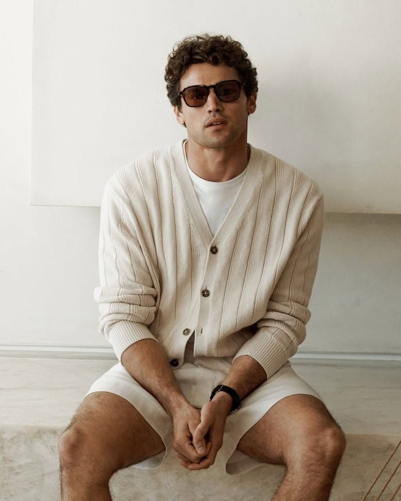 Giacomo wears a cream ribbed linen cardigan over a white T-shirt with linen shorts and square tortoise sunglasses for Calvin Klein spring 2026