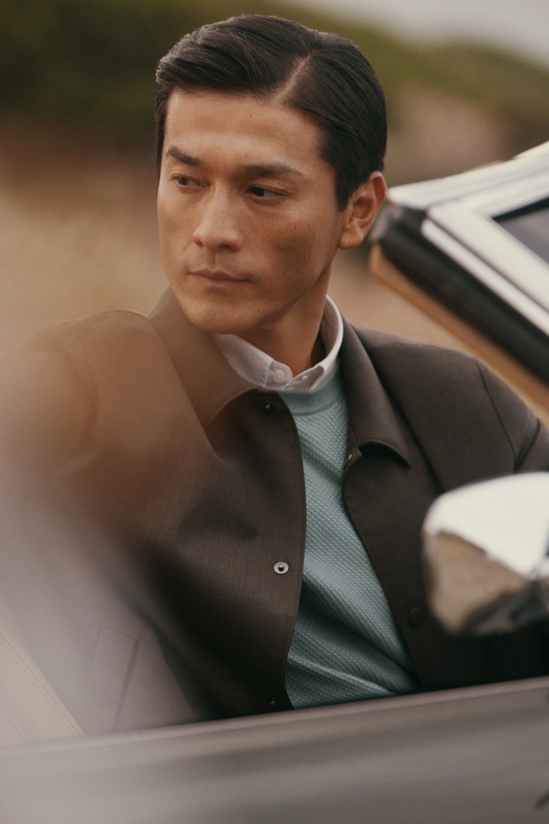 Daisuke sits behind the wheel of a vintage car in a snap jacket layered over a teal knit and white shirt for Canali's spring-summer 2026 campaign
