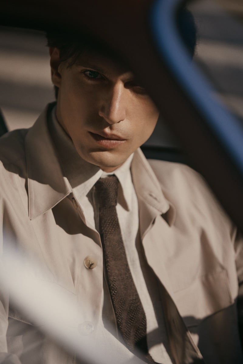 Edoardo sits inside a car in a light tan jacket with a muted brown knit tie and shirt, lit by low sunlight, for Canali's spring-summer 2026 campaign