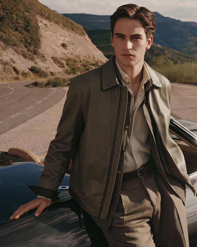 Luca leans on the hood of a vintage car along a mountain road in a zip jacket open over a light shirt for Canali's spring-summer 2026 campaign