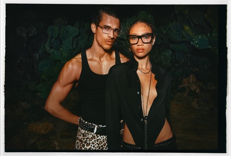 Jonas Barros in a black tank, leopard print trousers, and studded belt stands beside a female model in a sheer black shirt at night against a wall of cacti for Dsquared2's spring-summer 2026 campaign