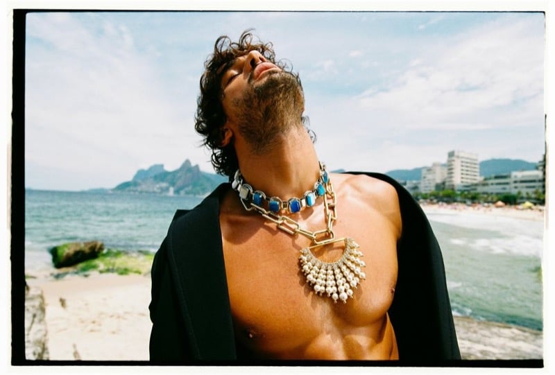 Marlon tilts his head back on the beach with a black blazer slipping off his shoulders, layered chunky jeweled chains and a pearl pendant across his bare chest, for Dsquared2's spring-summer 2026 campaign