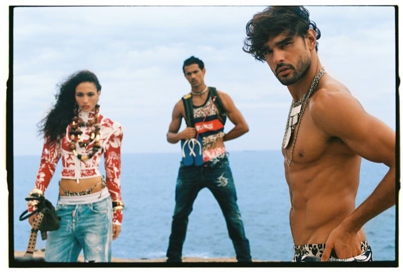 A female model in a red Hawaiian print top stands beside Jonas Barros in a red graphic tank, while Marlon stands shirtless in animal-print swim shorts in the foreground for Dsquared2's spring-summer 2026 campaign