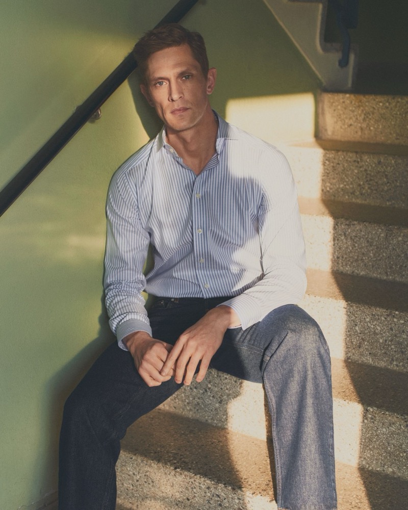 Mathias sits on factory stairs in a striped Eton poplin shirt