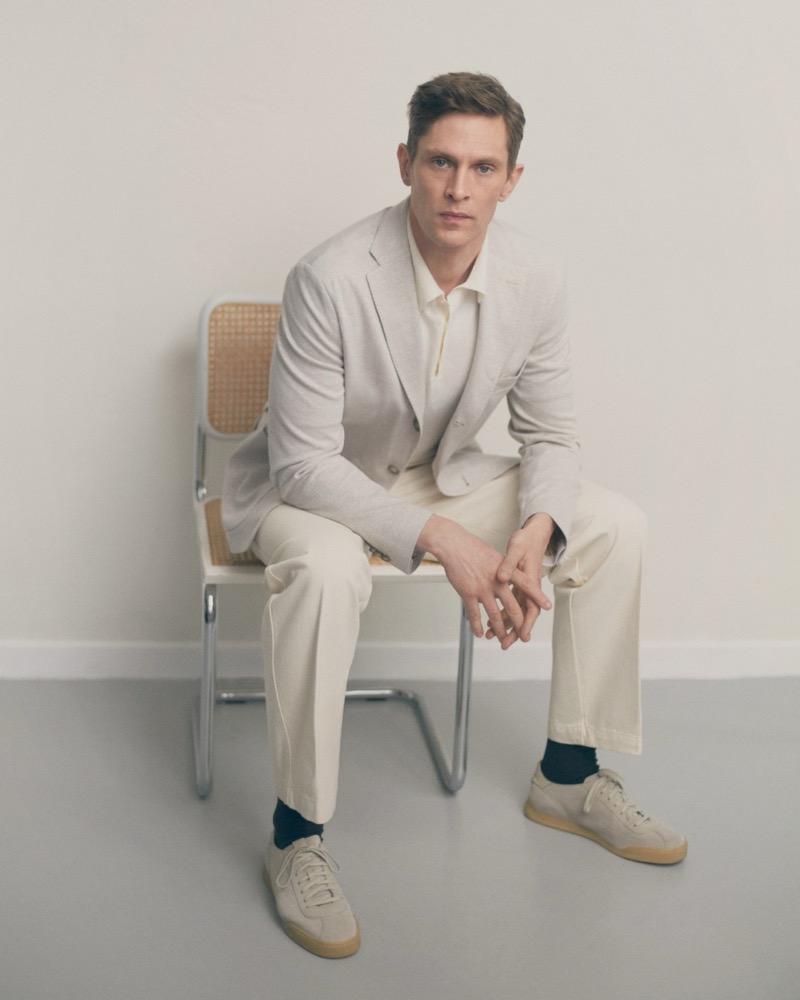 Mathias sits in a cream Eton unstructured blazer with suede sneakers