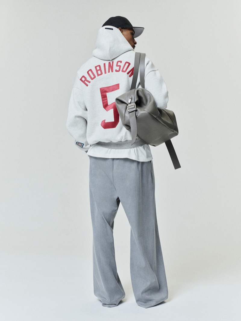Rear view of the Fear of God Essentials NLBM sport hoodie with Robinson 5 lettering in red, paired with grey trousers and a leather bag