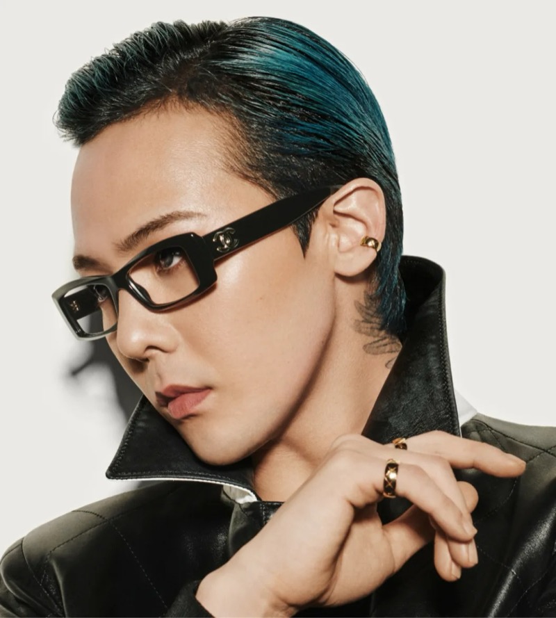 G-Dragon wears slim Chanel black rectangle eyeglasses with the gold double C logo on the arm, layered over a black leather jacket with a popped collar
