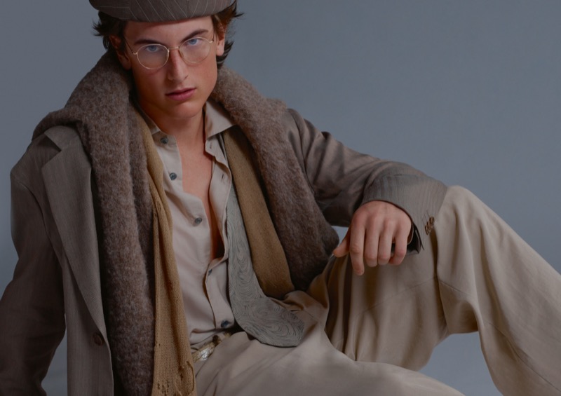 Sean sits in a light neutral suit layered with a mohair sweater, shirt, tie, flat cap, and clear aviator glasses for Giorgio Armani's ARMANI/Archivio 2026 campaign