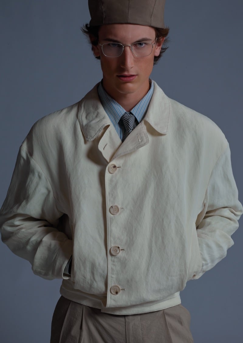 Sean wears a jacket over a blue striped shirt and navy striped tie, paired with a brown soft cap and clear eyeglasses, for Giorgio Armani's ARMANI/Archivio 2026 campaign