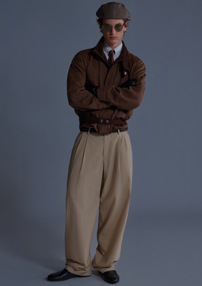 Sean wears a belted brown bomber jacket with a white shirt, patterned tie, leather gloves, high-waisted khaki trousers, brown cap, and round sunglasses for Giorgio Armani's ARMANI/Archivio 2026 campaign