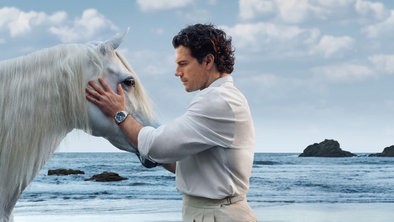 Cavill stands with a white horse on the beach wearing the Longines HydroConquest