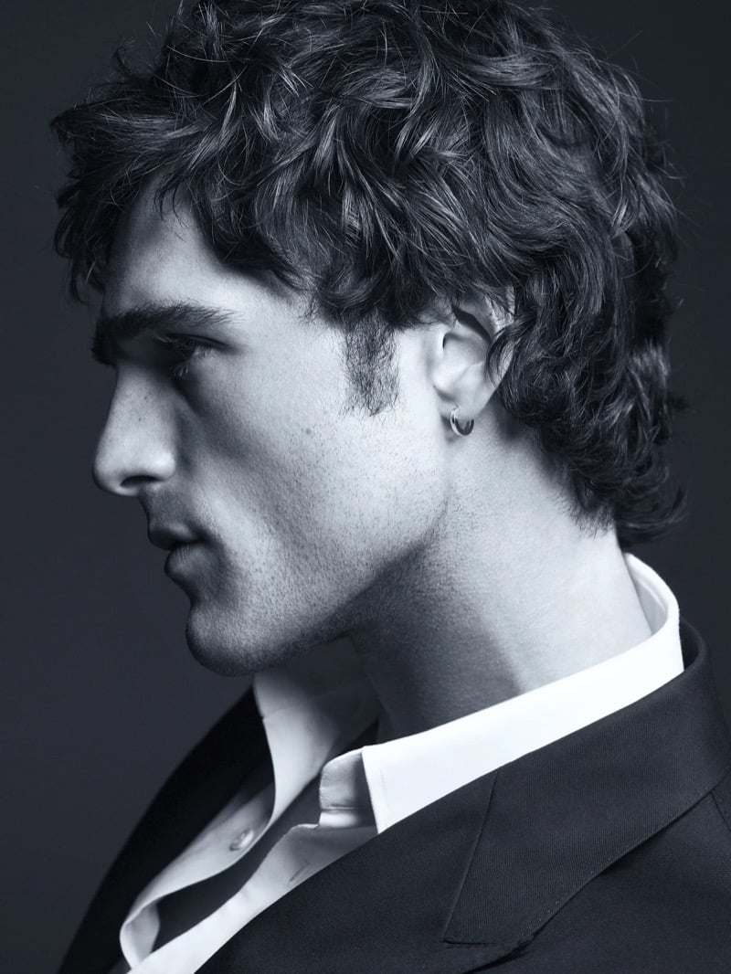 Black-and-white profile portrait of Elordi in a dark suit jacket and open white shirt with a small hoop earring for Bleu de Chanel