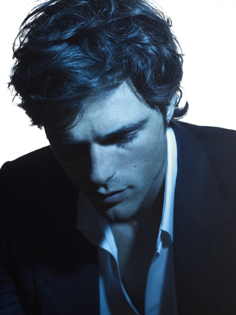 Blue-toned portrait of Elordi looking down, with tousled dark hair and a dark suit jacket over a white shirt for Bleu de Chanel 