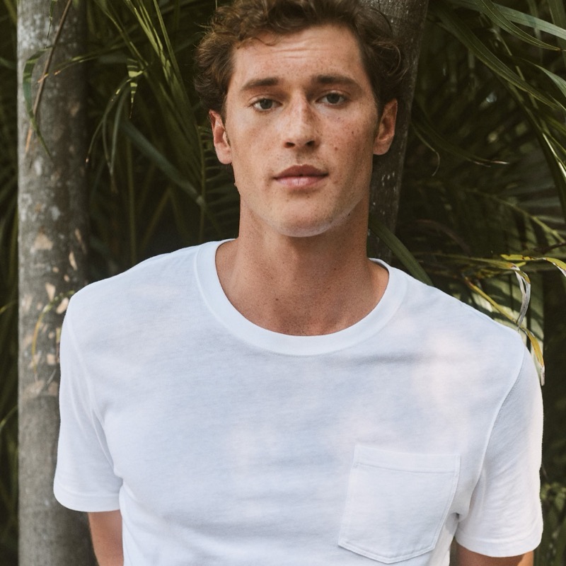 Jacques wears a white pocket T-shirt in front of palm fronds