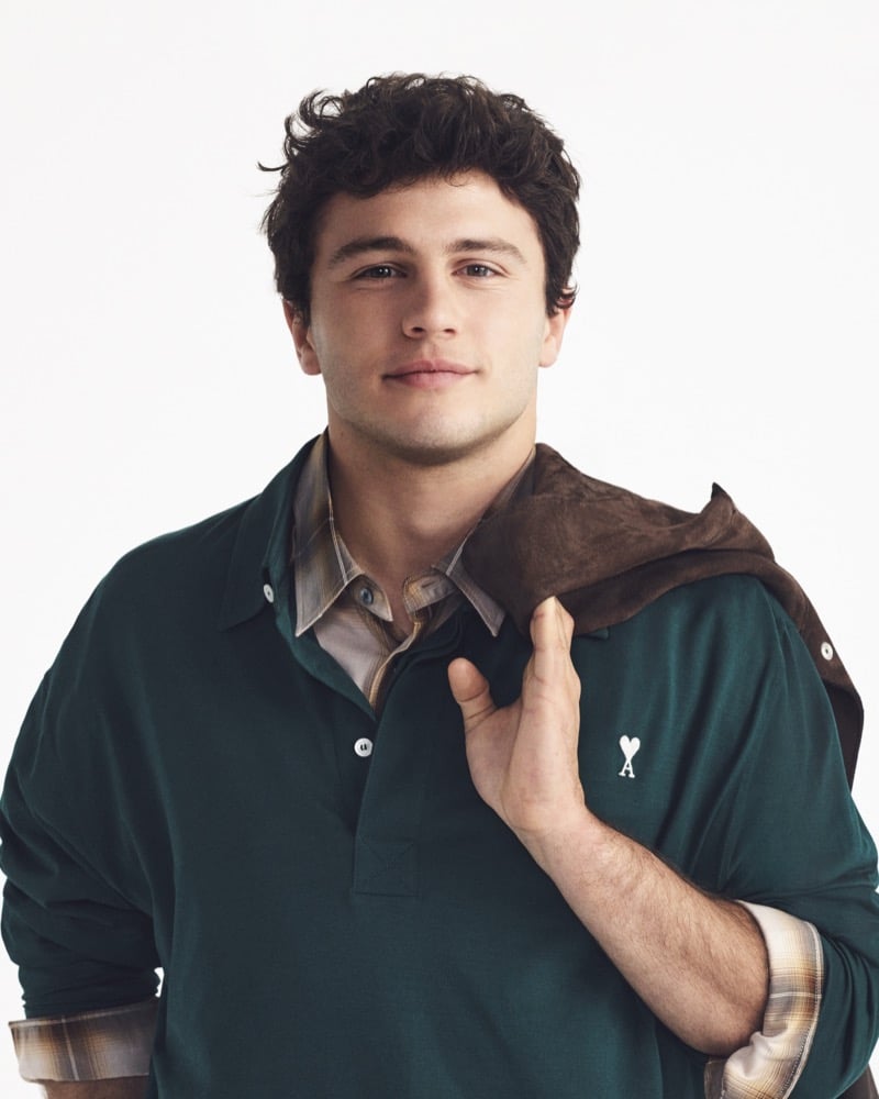 Close-up portrait of João Neves in a green Ami Paris long-sleeve polo with a brown suede overshirt slung over one shoulder