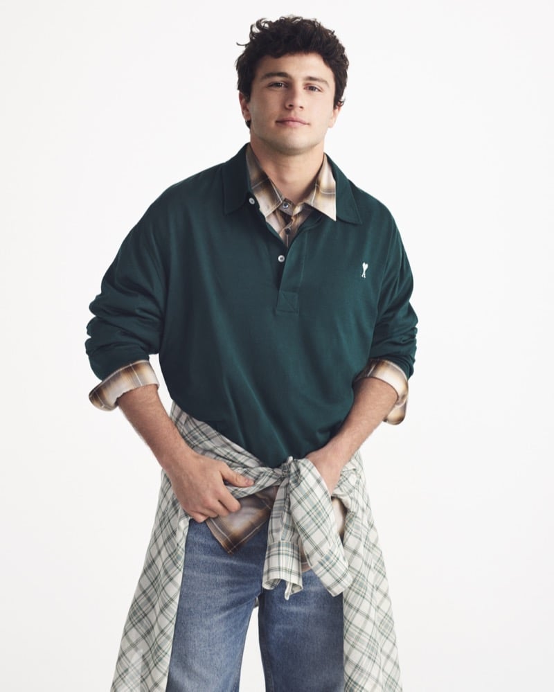 João Neves wears a green Ami Paris long-sleeve polo with a tan plaid flannel underneath and a green check flannel tied at the waist over blue jeans