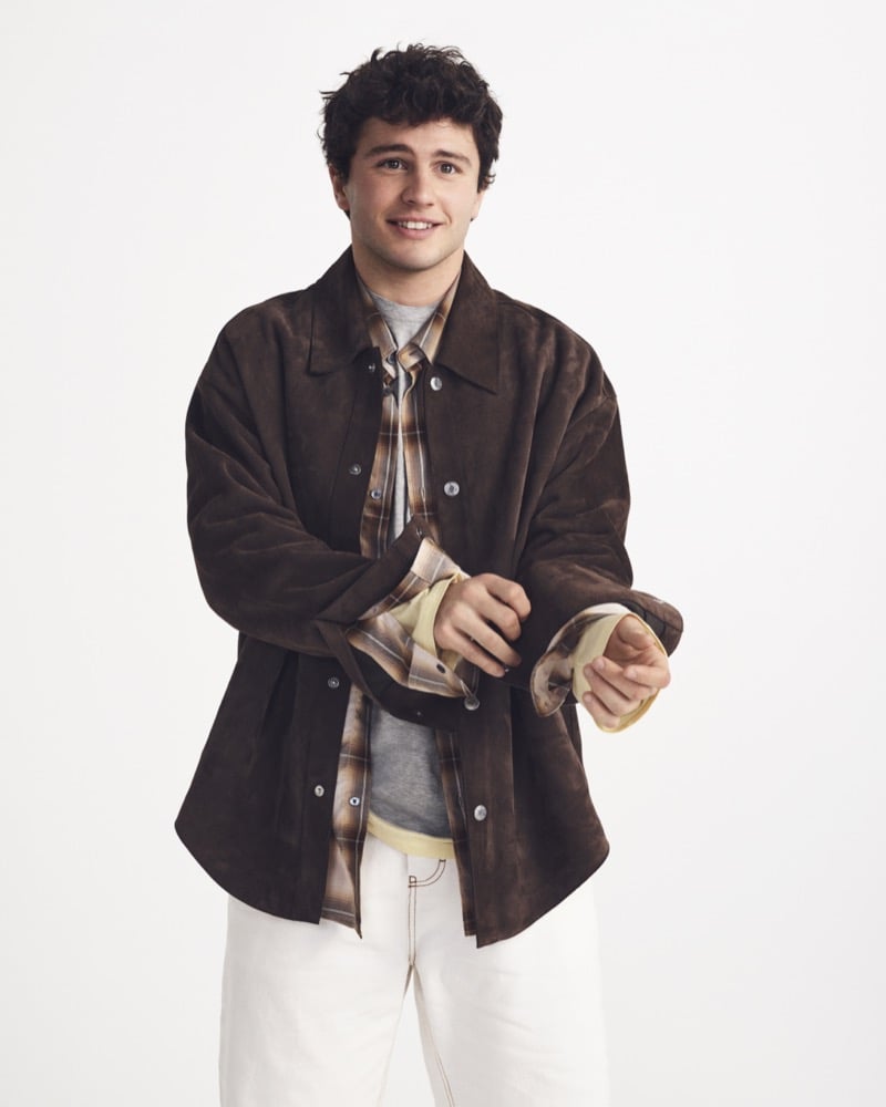 João Neves cuffs the sleeve of a brown Ami Paris suede overshirt worn over a plaid flannel, gray tee, and cream denim trousers