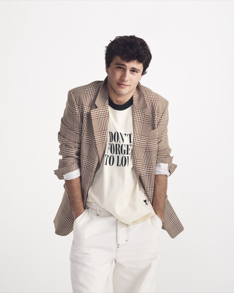 João Neves wears a brown gingham Ami Paris blazer over a cream "Don't Forget to Love" graphic t-shirt with white denim trousers