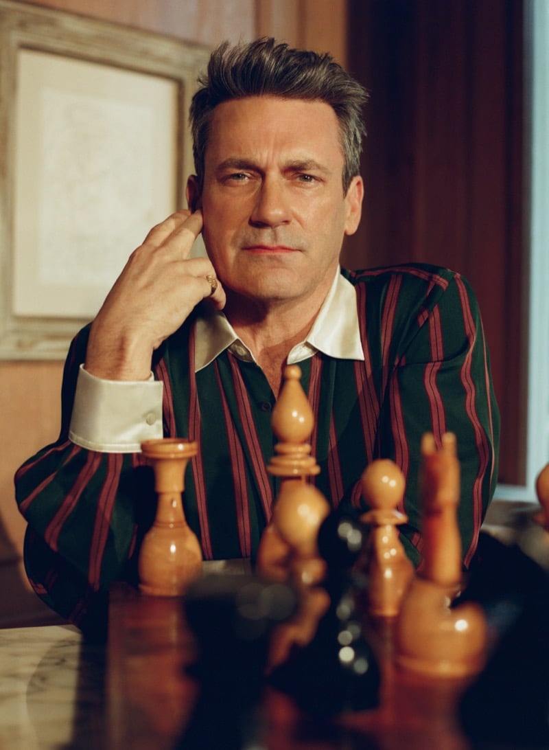 Jon sits at a chess table wearing a dark green and burgundy striped silk shirt with French cuffs