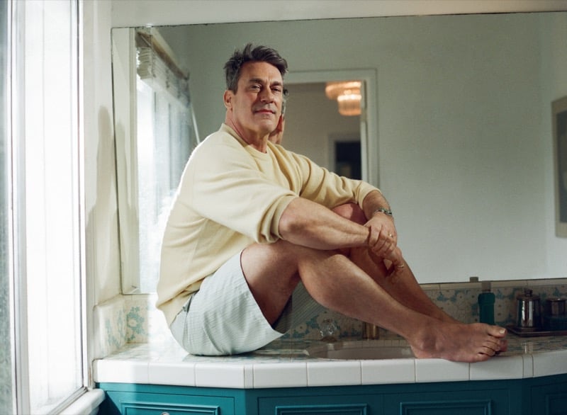 Jon sits on a bathroom counter wearing a cashmere sweater and striped drawstring shorts